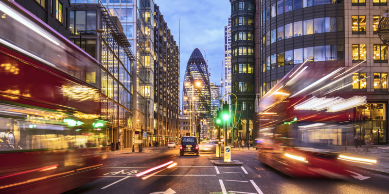 Financial district in London at dusk with buses driving through.