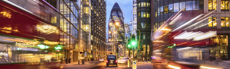 Financial district in London at dusk with buses driving through.