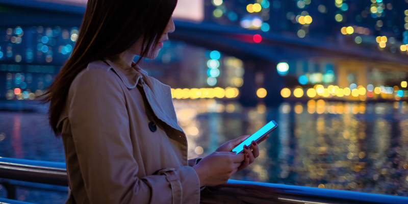 Beautiful lady relaxing by the pier and using smartphone at dusk