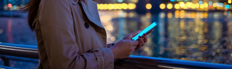 Beautiful lady relaxing by the pier and using smartphone at dusk