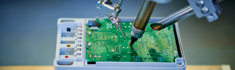 Robotic arm welding and installing component at semiconductor circuit board on workbench.