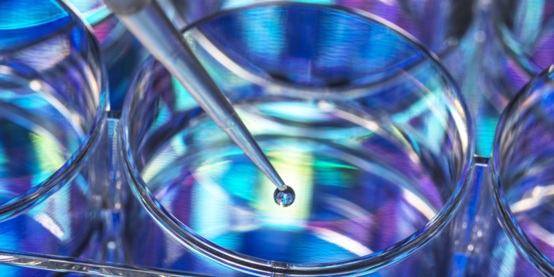 Pipetting a DNA (deoxyribonucleic acid) sample into a multiwell plate with DNA information in the background