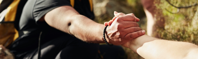 Cropped shot of two young women reaching for each other's hands on a hiking trail