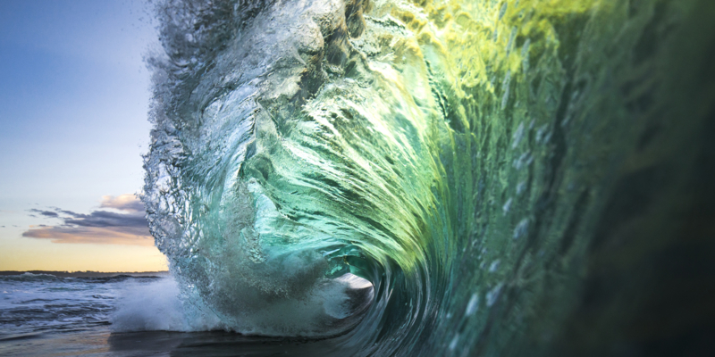 Large colourful wave breaking in ocean over reef and rock